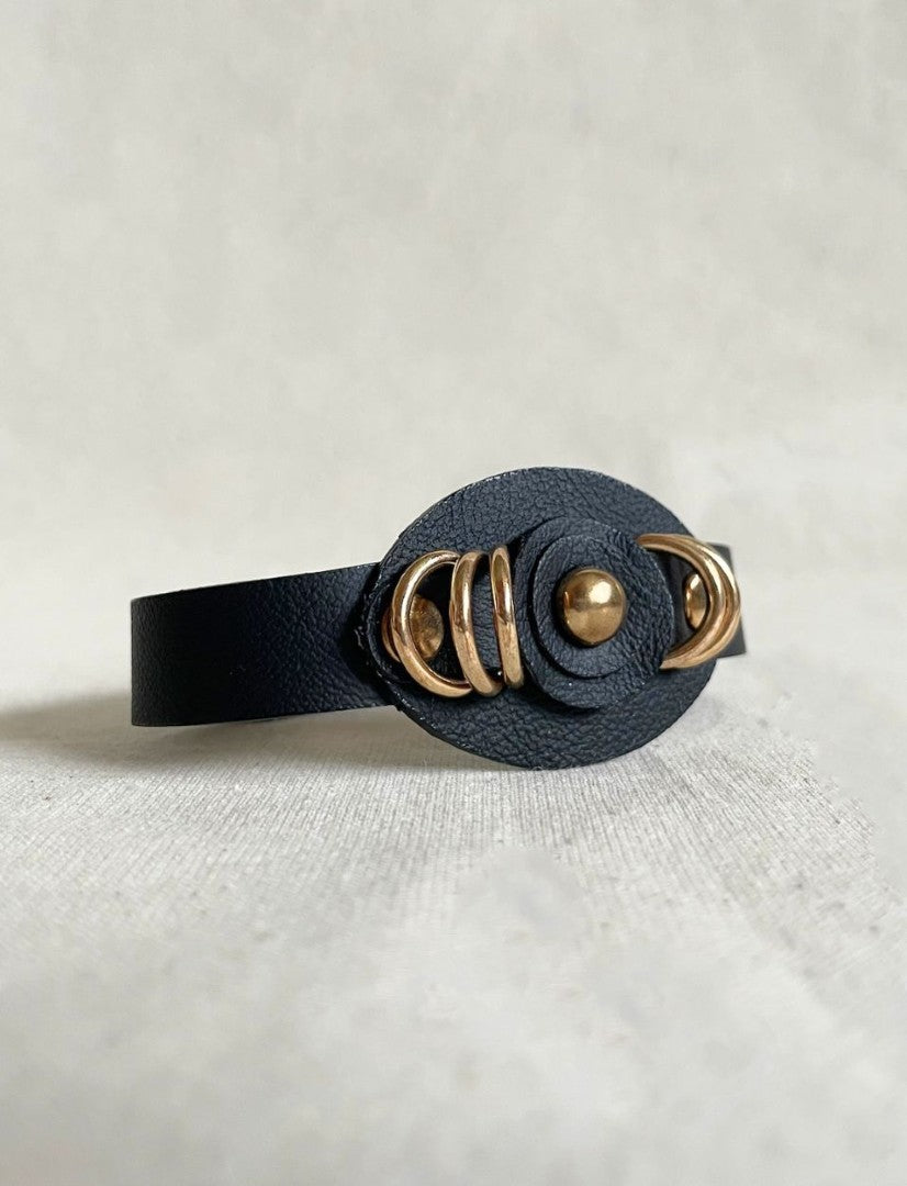 Black leather bracelet with gold circular accents on a light gray background