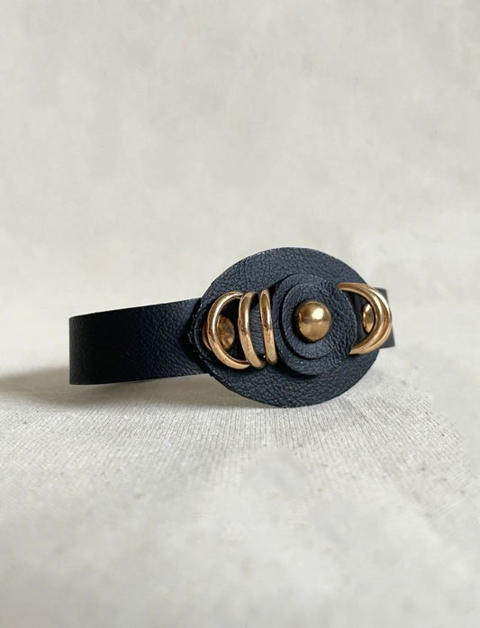 Black leather bracelet with gold circular accents on a light gray background